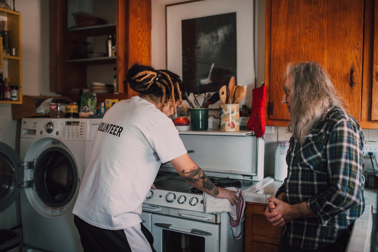 A volunteer helps an elderly person in a cozy kitchen, promoting community kindness.